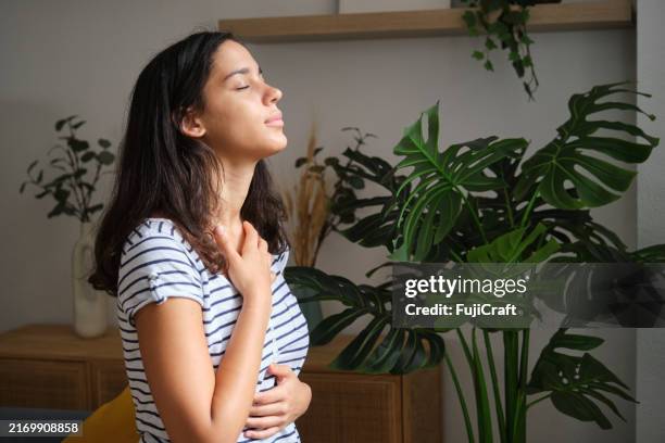 mujer joven practicando ejercicio de respiración profunda en casa - organismo-vivo fotografías e imágenes de stock