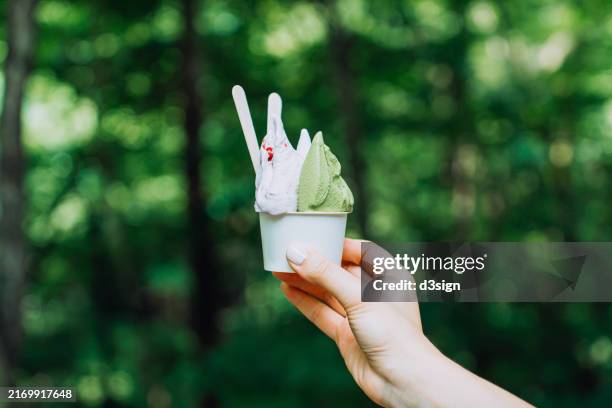 cropped shot of a female hand holding gelato in a cup outdoors, against green nature with sunlight. it's summer! a refreshing treat - mr whippy ice cream stock pictures, royalty-free photos & images