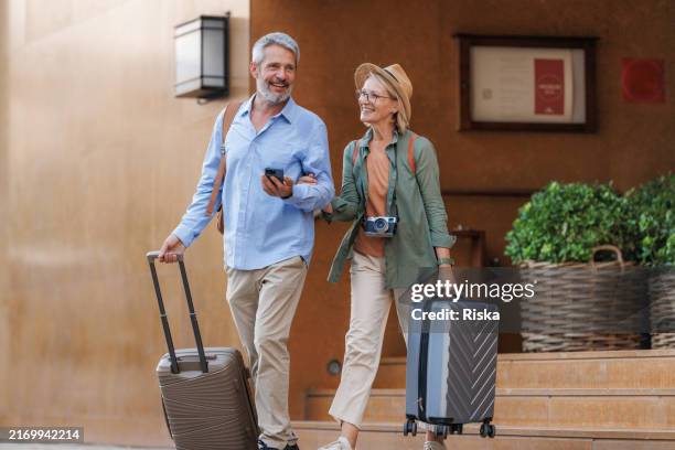 mature couple leaving a hotel with luggage on a city break - travel insurance stock pictures, royalty-free photos & images