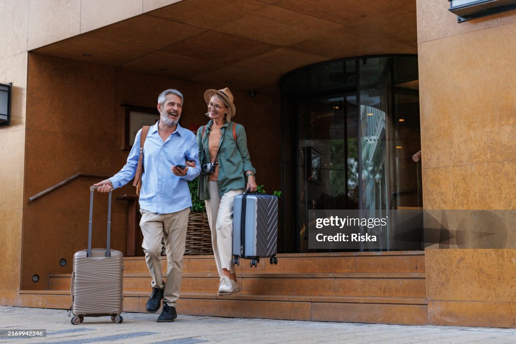 Smiling senior couple traveling and leaving hotel building