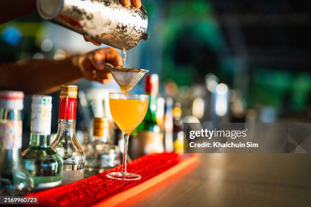 bartender's hand pouring cocktail into a glass at bar counter - cocktail party foto e immagini stock