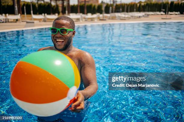 young adult having fun at public swimming pool holding beach ball in water - beach ball stock pictures, royalty-free photos & images
