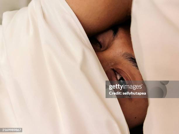 young man hiding in bed behind duvet - bettdecke stock-fotos und bilder
