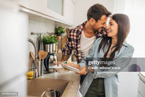 young cheerful couple washing the dishes in the kitchen. - washing dishes stock pictures, royalty-free photos & images