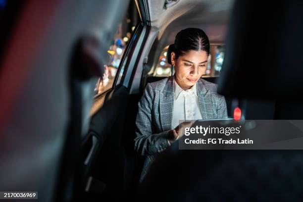 mid adult businesswoman using digital tablet inside a taxi - millennial traveler business stock pictures, royalty-free photos & images