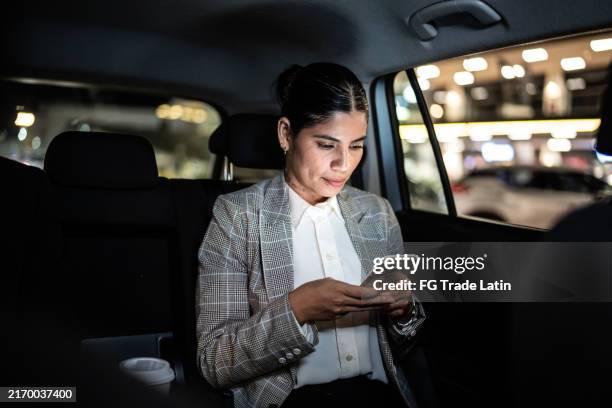 mujer de negocios adulta media usando el teléfono móvil dentro de un taxi - viaje de negocios fotografías e imágenes de stock