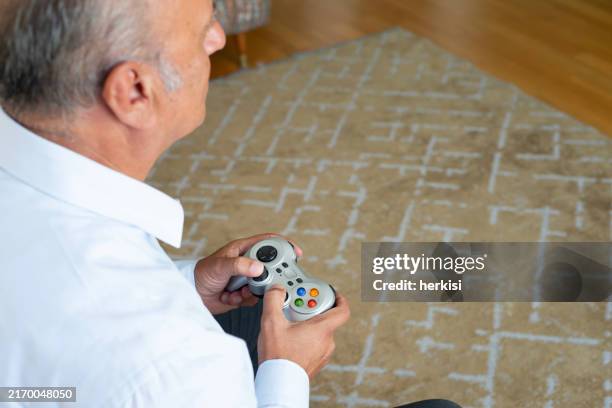 älterer mann, der videospiel auf playstation genießt und spaß zu hause hat - gamepad stock-fotos und bilder