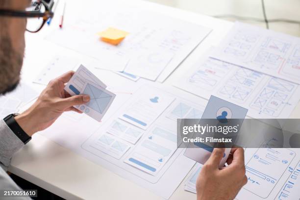 ux/ui designer working on wireframes for a website and mobile app prototype, surrounded by sketches of user-flow and design tools, in concept of website and mobile application design concept. - website wireframes stock pictures, royalty-free photos & images