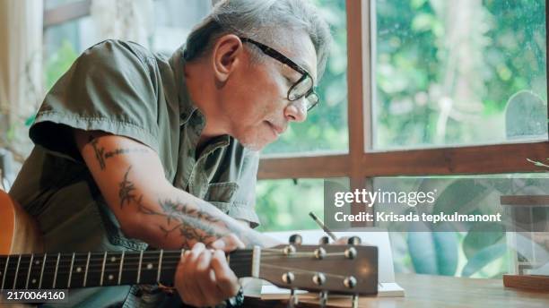 elderly asian man writing an acoustic song in the living room after retirement. - plucking an instrument stock pictures, royalty-free photos & images