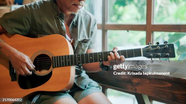 asiatischer mann im ruhestand, der das alter verbringt, um zu üben und akustische lieder im haus zu kreieren. - akustikgitarre stock-fotos und bilder