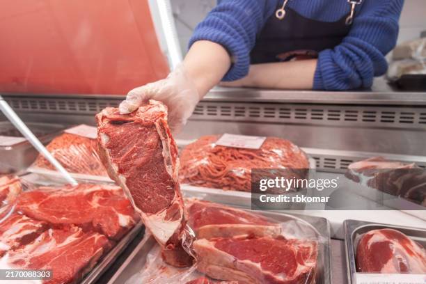 vendor holding raw beef steak above meat counter in a butcher shop - carnicero fotografías e imágenes de stock