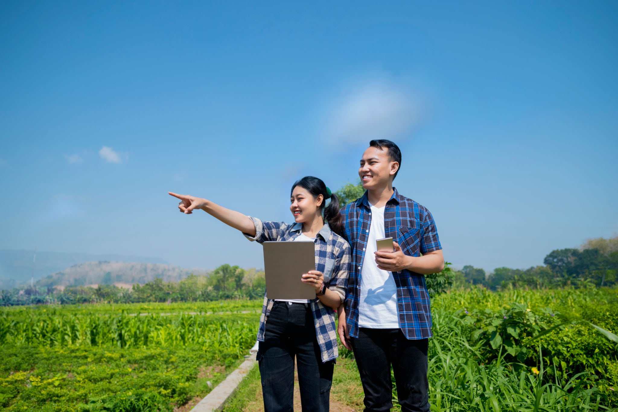 A man and a woman are looking at a tablet in a field A man and a woman are looking at a tablet in a field