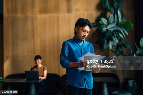 focused professional reviewing documents in modern office setting - blue shirt stock pictures, royalty-free photos & images