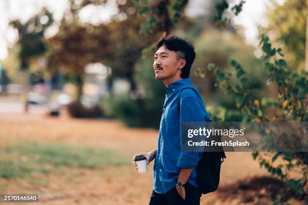 young asian man enjoying autumn day in a peaceful park setting - walking city stock pictures, royalty-free photos & images