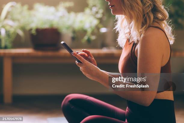 woman in workout outfit using smartphone in bright room - athleisure stock pictures, royalty-free photos & images
