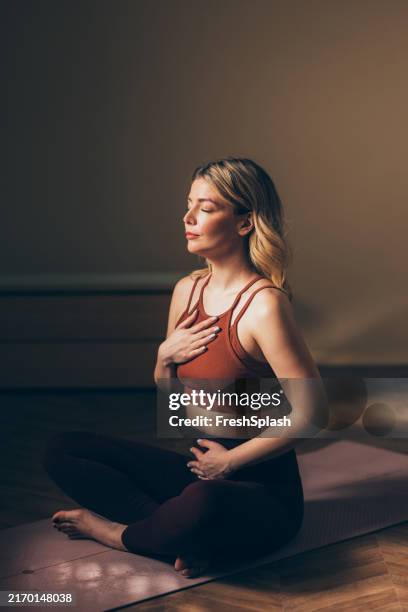 woman practicing meditation and mindfulness on yoga mat - lichaamshouding stockfoto's en -beelden