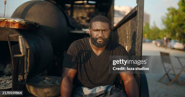 bearded food truck owner resting by outdoor smoker after a day of barbecuing - smokehouse stock pictures, royalty-free photos & images