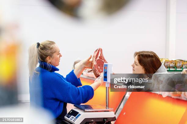 market worker showing a large beef steak to a customer at the counter - viande rouge photos et images de collection