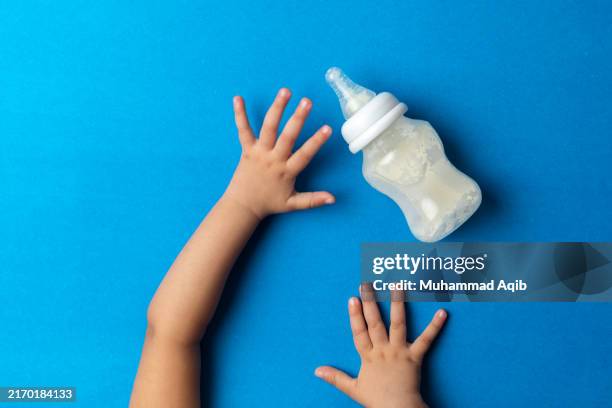 a toddler reaching for milk feeding bottle - milchflasche stock-fotos und bilder