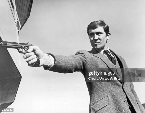 Promotional portrait of Australian actor George Lazenby aiming a gun for the James Bond film, 'On Her Majesty's Secret Service,' directed by Peter...