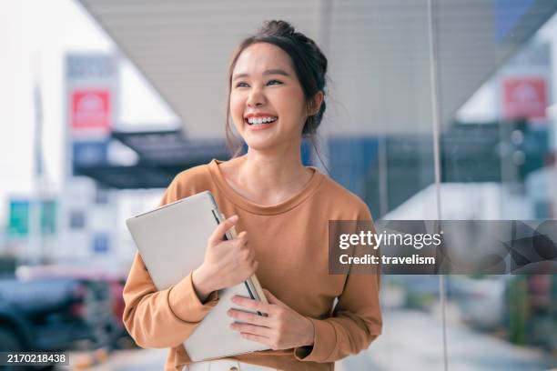 lächelnd begrüssung fröhlich asiatisch teen frau positiv freundlich willkommen hand halten laptop dokument akte ordner gehen mit sorglos freizeit outdoor store ladenfront daytime - funkwelle stock-fotos und bilder