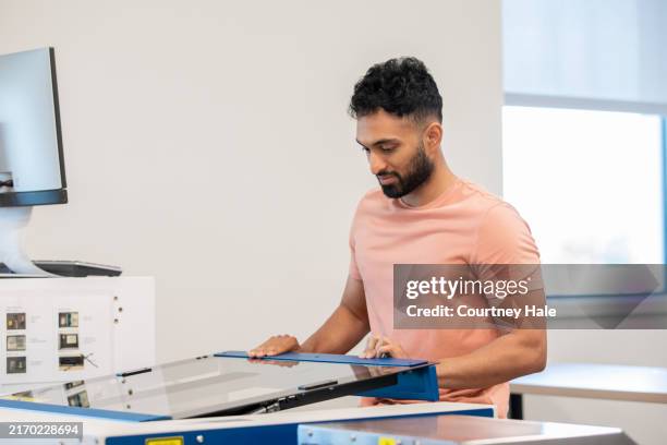 young man uses laser engraver in stem lab - laser engraving stock pictures, royalty-free photos & images