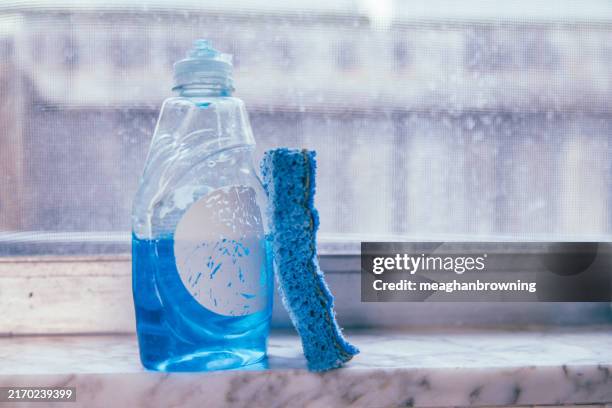 close-up of a blue sponge on a window sill next to a bottle of washing up liquid - washing up liquid stock pictures, royalty-free photos & images