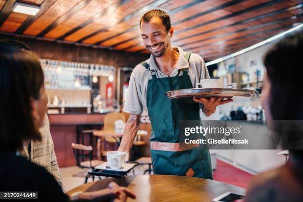 waiter serving group of friends in a cafe - ober stockfoto's en -beelden