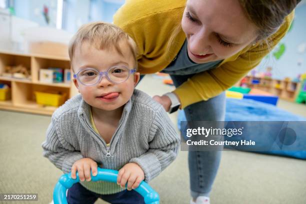 little boy with down syndrome smiles while playing in daycare play room at preschool - neurologische aandoening stockfoto's en -beelden