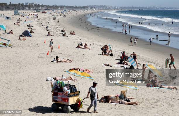 Vendor pulls a cart carrying beach umbrellas and other items for sale as people gather on Santa Monica Beach on September 04, 2024 in Santa Monica,...