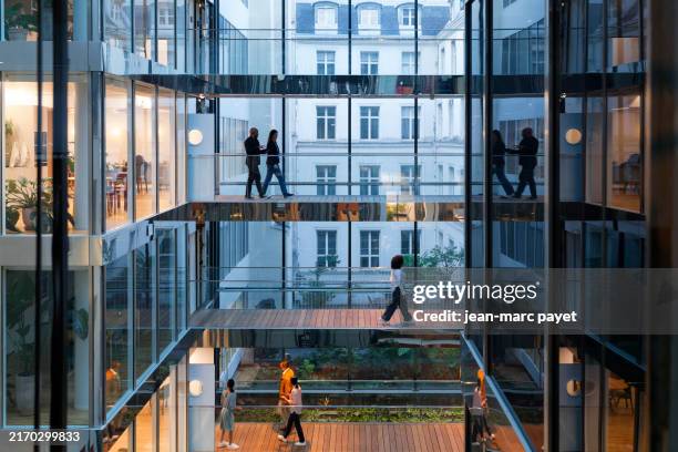modern office building with silhouette of business women and men crossing a raised bridge on several levels in a company located in paris - quartier de bureaux photos et images de collection