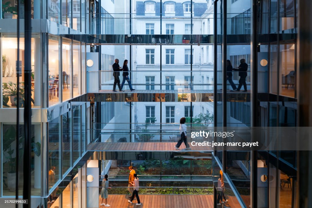 Modern office building with silhouette of business women and men crossing a raised bridge on several levels in a company located in Paris