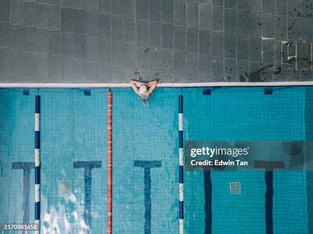 drone point of view asian chinese female swimmer resting at edge of swimming pool - zwembadlaan scheidingslijn stockfoto's en -beelden