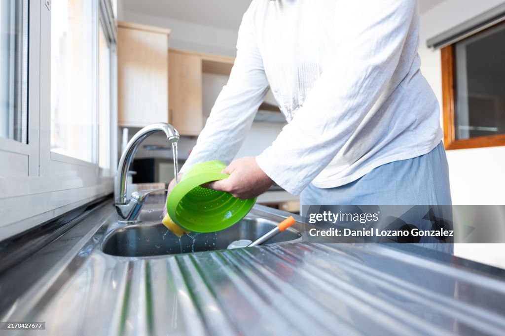 Man washing green colander in kitchen sink