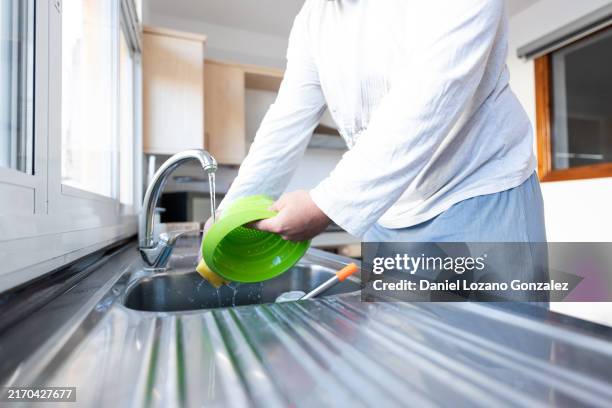 man washing green colander in kitchen sink - spülmittel stock-fotos und bilder