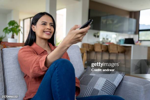 donna che guarda la tv a casa e cambia canale con il telecomando - telecomando foto e immagini stock
