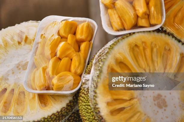 a half-cut fresh jackfruit and jackfruit meat are displayed in a plastic container and available for sale at the market. - cut jackfruit stock pictures, royalty-free photos & images