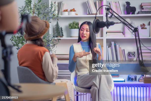 rear view of young asian woman with quest interview sitting together conversation discuss ideas sharing in home studio with lighting studio set up record lives straming into microphone while recording podcast - radio dj stock pictures, royalty-free photos & images