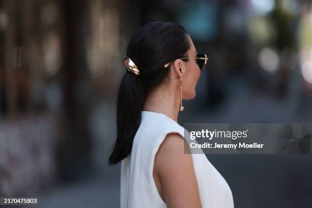Yana Echko seen wearing Iron Paris gold sunglasses, Jacquemus gold pendant earrings, Mango white elegant vest, gold metallic hair tie / clip, during...