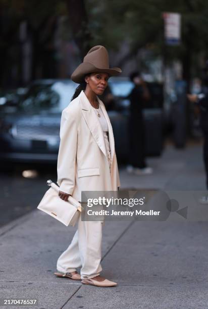 Fashion Week guest is seen wearing a tall, oversized brown felt hat with a curved crown and wide, turned-down brim; shiny stud earrings; two gold...