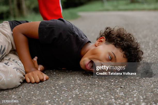 black boy fell on pavement in epileptic fit, lying on side with open mouth and rolling eyes while unseen dad standing behind. - bewusteloos stockfoto's en -beelden
