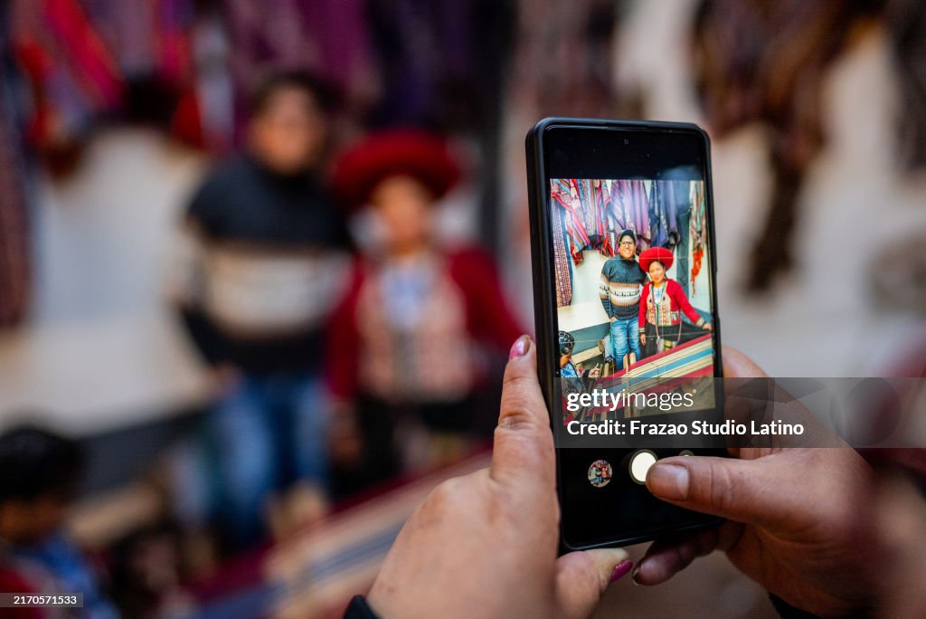 Close-up of a woman photographing chinchero indigenous and tourist with a mobile phone on a market, in Chinchero district, Peru