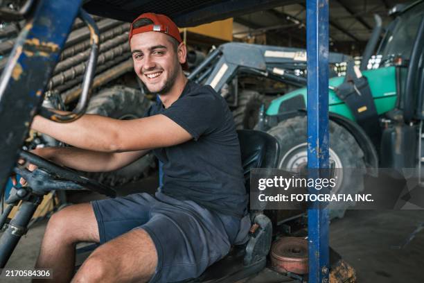 männlicher landwirt bedient gabelstapler die garage des bauernhofs am morgen - organischer bauernhof stock-fotos und bilder