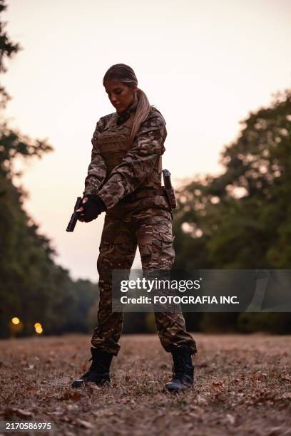 young armed female soldier handling handgun in wooded area during military training in sunset - gun control stock pictures, royalty-free photos & images