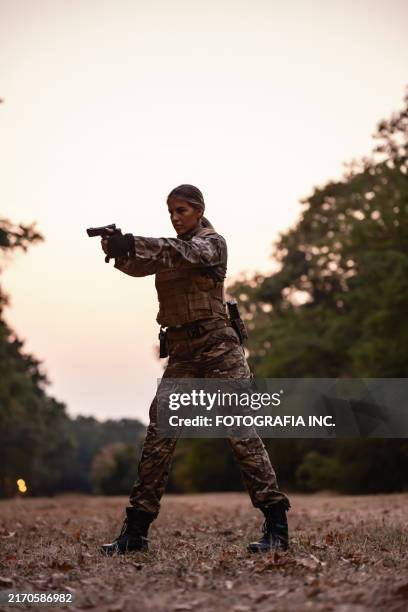 young armed female soldier handling handgun in wooded area during military training in sunset - gun control stock pictures, royalty-free photos & images