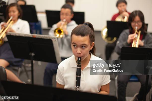 asian caucasian multiracial teenage girl junior high student playing clarinet instrument in band orchestra in school - klarinet stockfoto's en -beelden