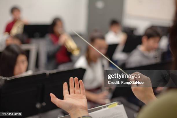 blick auf die band, den lehrer, den lehrer, den dirigentenhände, die das orchester der musikaufführung im orchester der mittelstufe leiten, die im klassenzimmer üben, zusammen in einer gruppe von menschen - dirigent stock-fotos und bilder