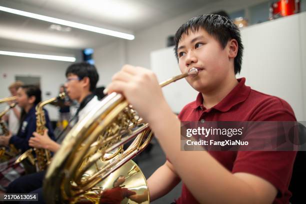 asian chinese teenage boy junior high student playing french horn in band class in school orchestra - blechblasinstrument stock-fotos und bilder