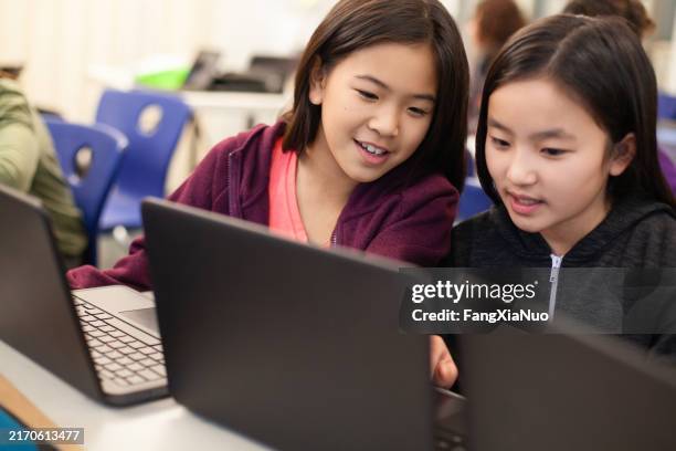 two asian chinese girls students collaborate together using laptop computer in elementary school classroom - kid coding stock pictures, royalty-free photos & images