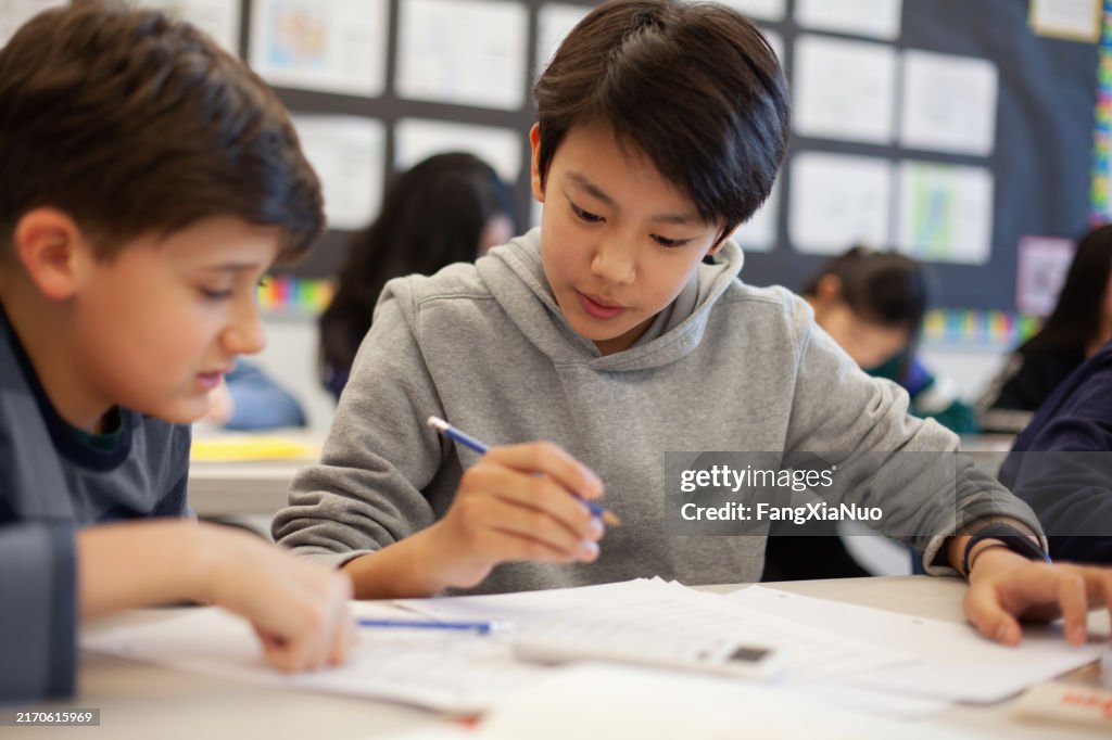 Asian multiracial Korean Japanese boy studies in elementary school classroom with classmate